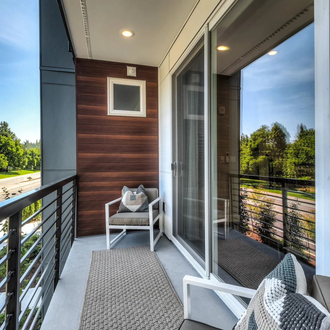 Two pale armchairs face inward along a narrow covered balcony beside sliding glass doors
