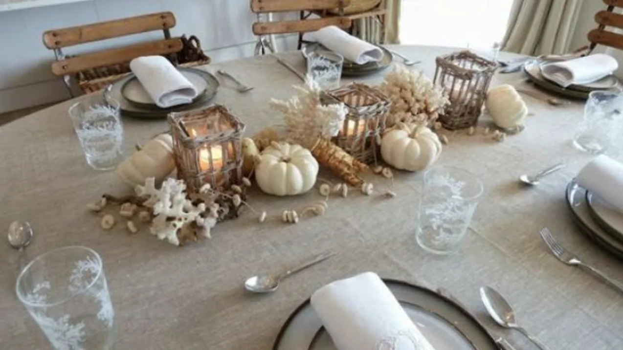 A pale dining table with gray plates and white napkins holds white pumpkins, shell and coral-shaped ornaments and low slatted candleholders