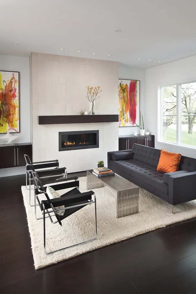 A dark gray sofa sits beside a white fireplace with an orange cushion at one end