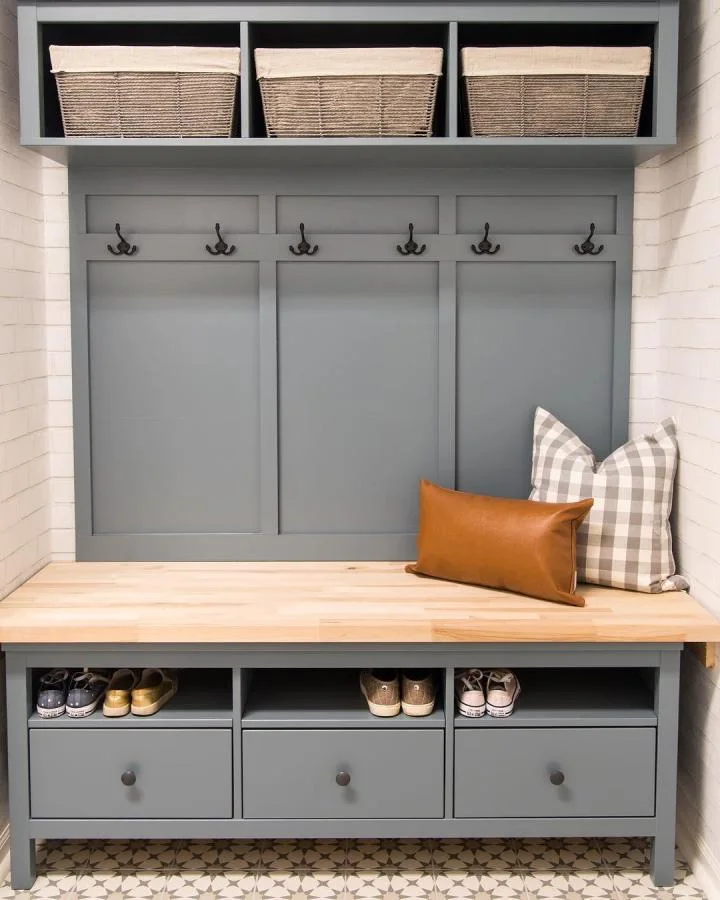 Blue-gray mudroom bench arrangement with a wood top, open shoe spaces, three drawers, dark hooks and fabric-lined upper baskets.
