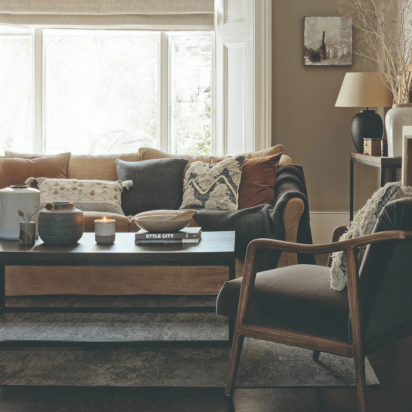 Light brown sofa with pale patterned, dark gray, textured geometric and rust pillows.