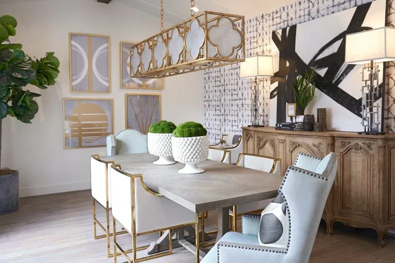 Carved wood dining sideboard beneath large artwork and two lamps behind pale blue chairs and a gray table