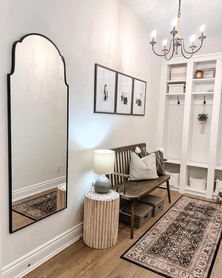 Wood bench and a tall mirror opposite white beadboard-backed storage cubbies with black hooks and round baskets.