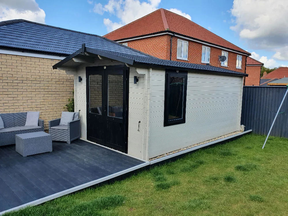 Pale garden pub cabin with dark glazed doors beside a small paved seating terrace