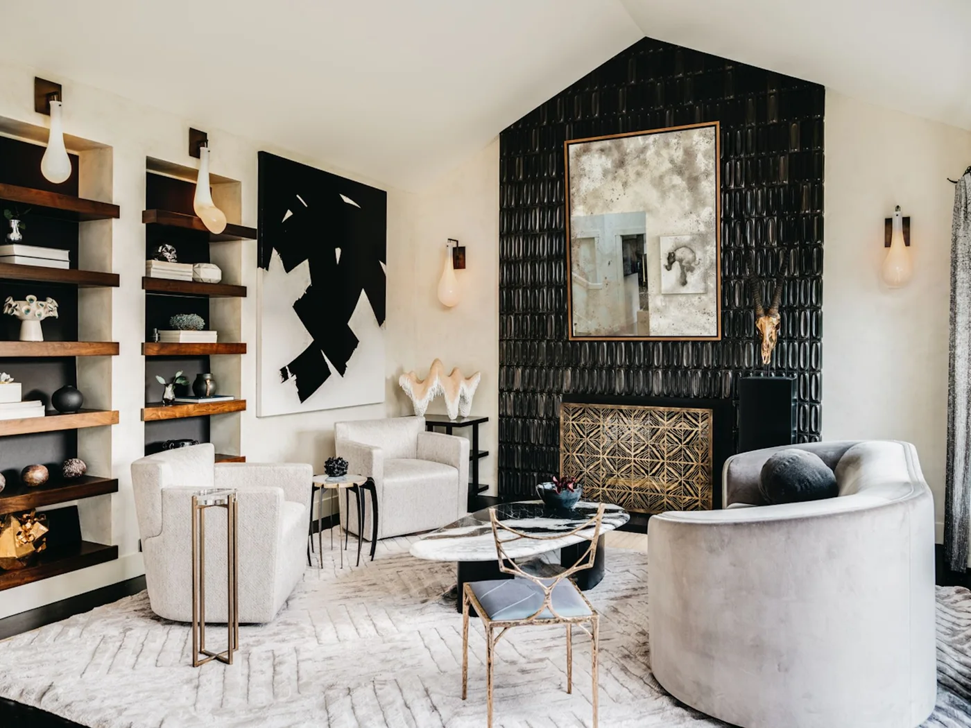 Glossy black relief tiles cover a fireplace beneath a tall mirror, with a patterned fire screen, pale curved seating and wood shelves.
