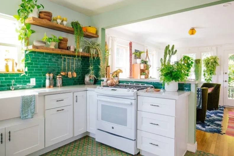 Green rectangular tiles sit behind wooden open shelves and pale lower cupboards beside a white cooker and hanging utensils
