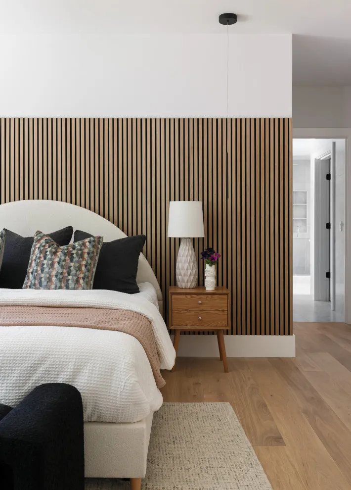 Vertical timber slats form a warm panel behind a pale bed and dark cushions