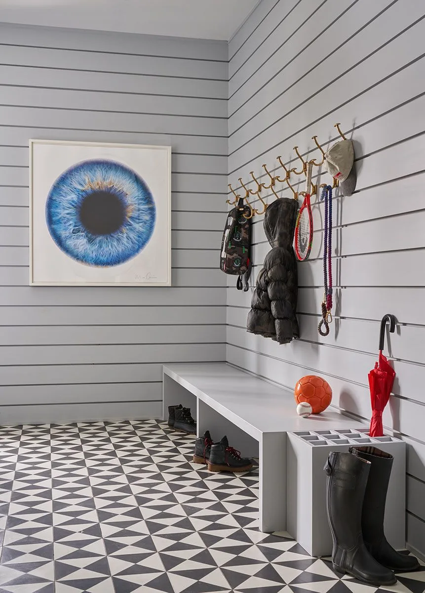 Gray paneled entry with long wall hooks, a low bench, divided umbrella holder and black-and-white geometric floor