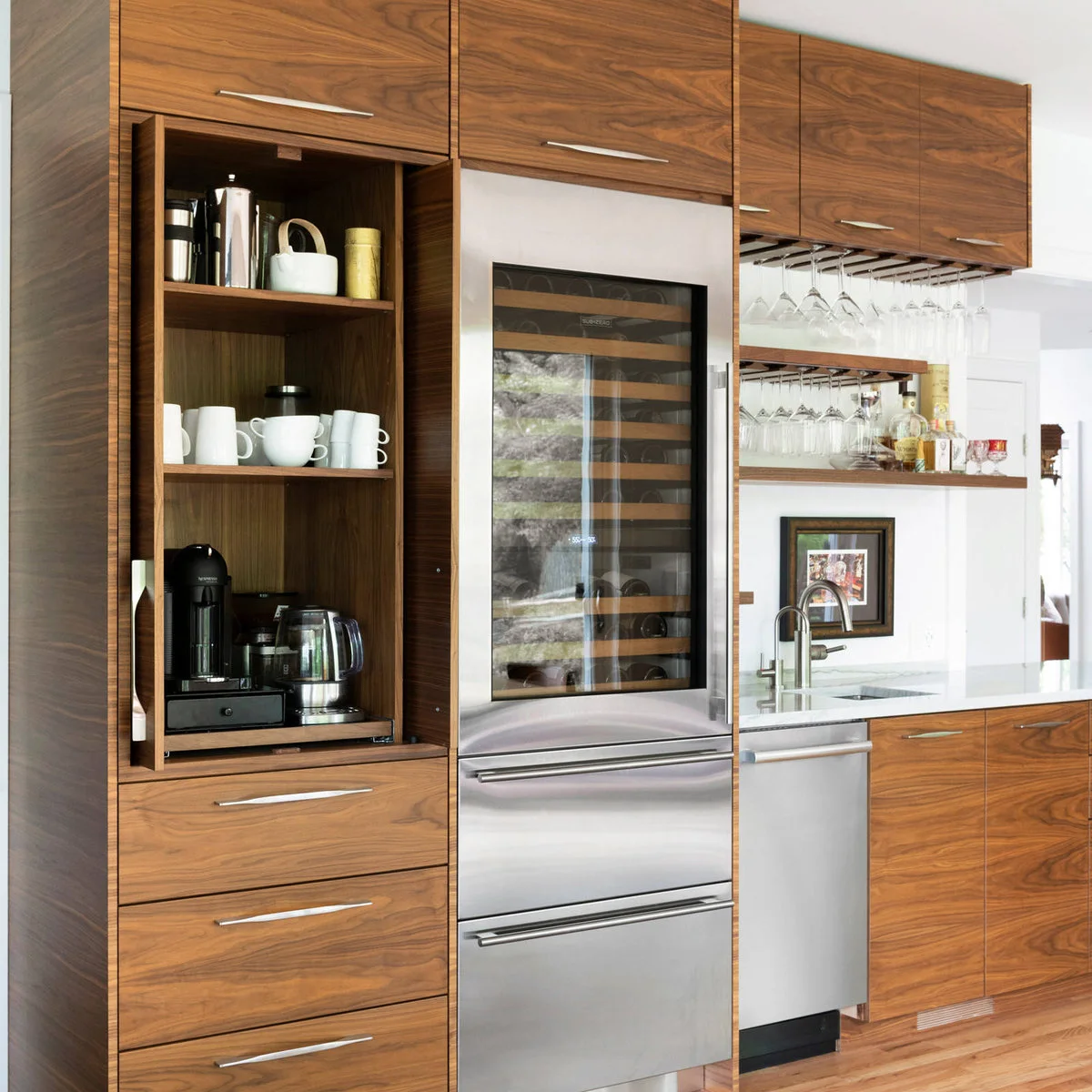 Wood-grain flat-front cupboards sit above a tall glass-front wine refrigerator beside a coffee station.