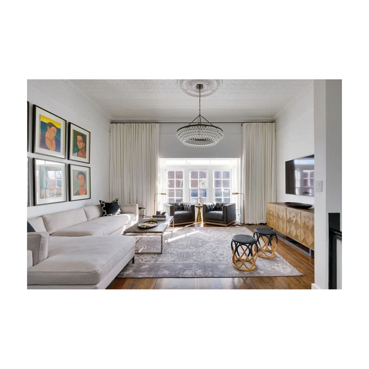 Narrow living room with a pale sectional, two dark chairs by the window and a television above a patterned cabinet