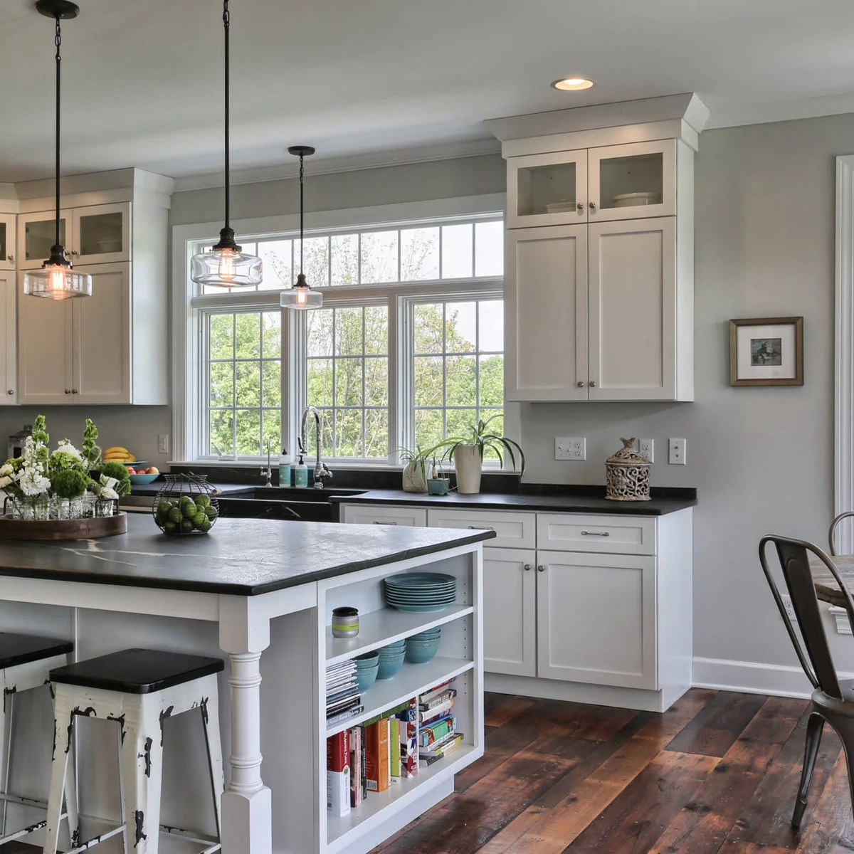 A broad divided kitchen window above a sink, flanked by white cabinets with smaller glass-fronted upper doors.