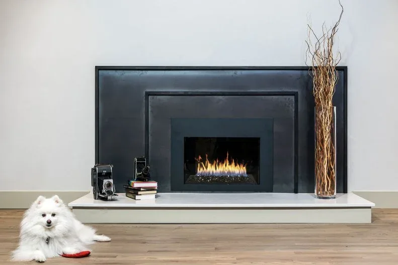 Black fireplace surround above white floating hearth with vintage cameras and tall branch-filled vase