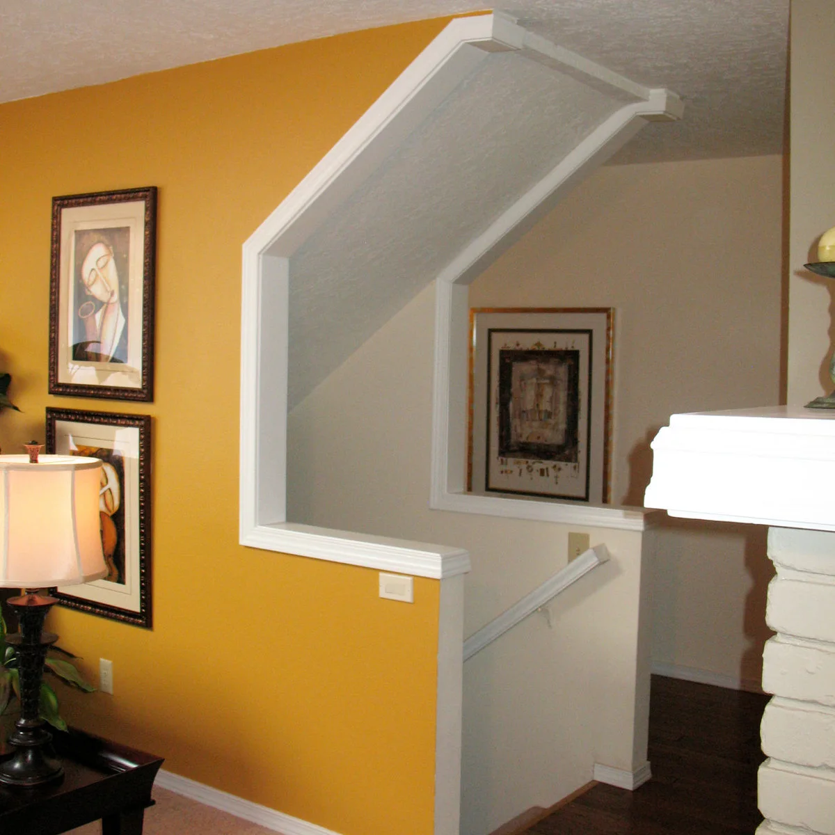 Yellow living room accent wall with framed pictures beside white stair trim and a pale adjoining hall