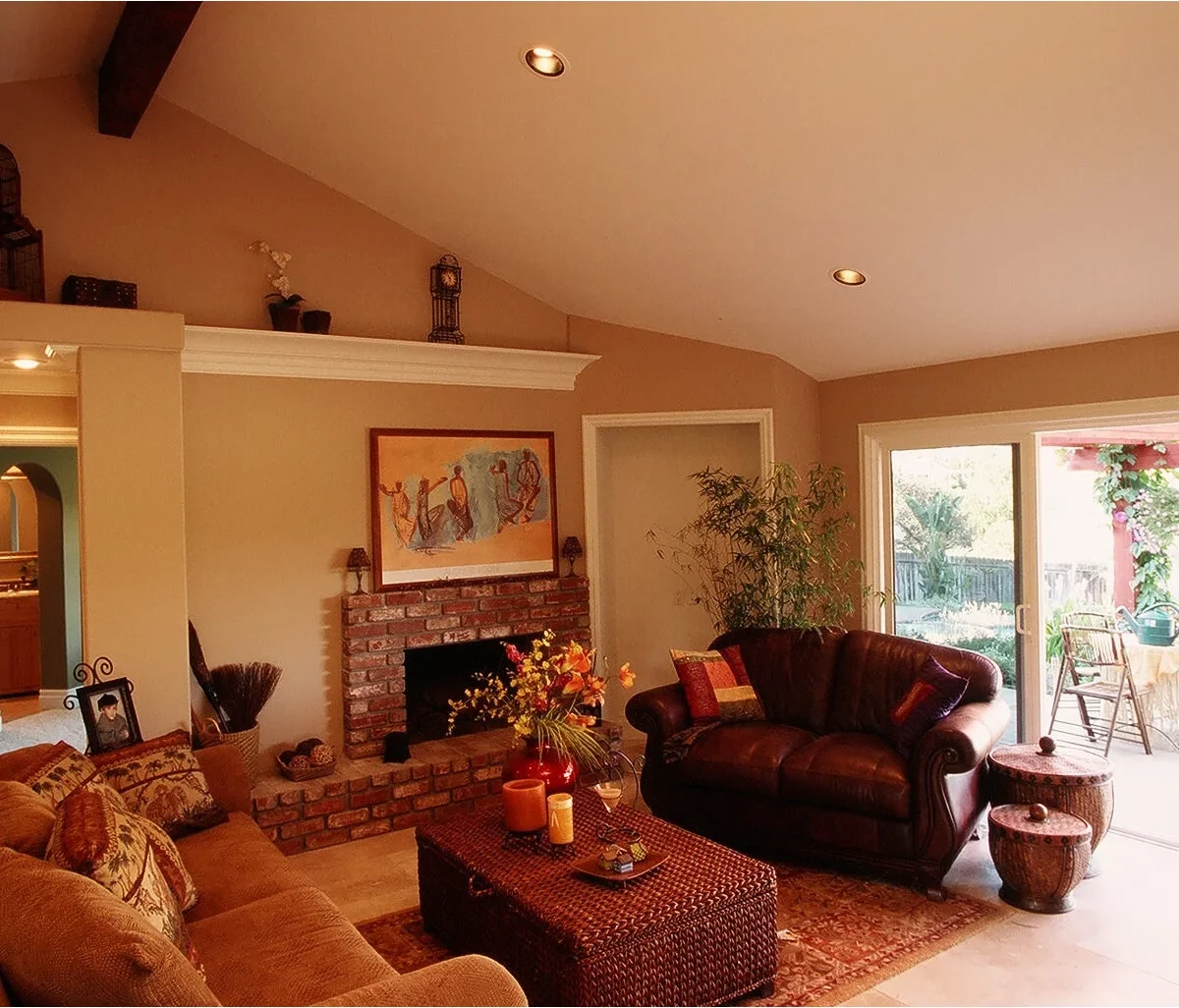 A red brick fireplace sits against warm tan walls beside dark leather seating, a woven coffee table and patterned textiles.