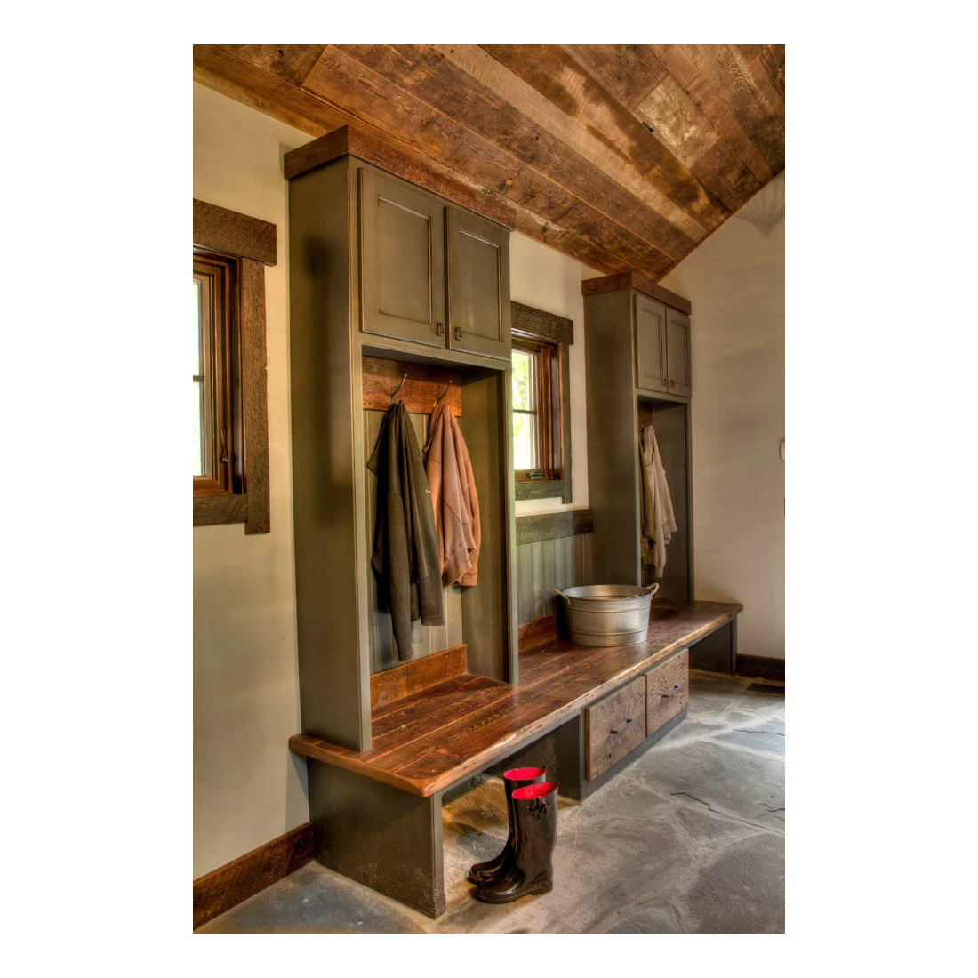Olive painted coat storage and upper cupboards above a timber bench on an irregular stone floor