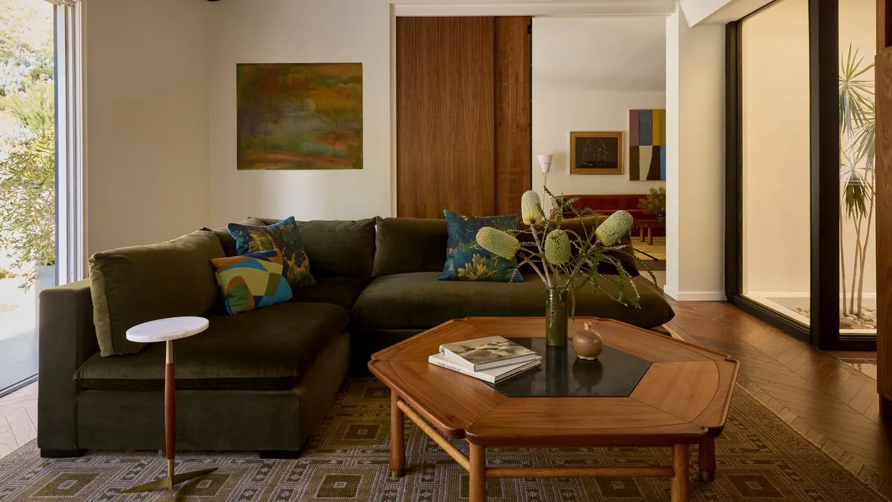 An olive sectional faces a timber coffee table in a light room.