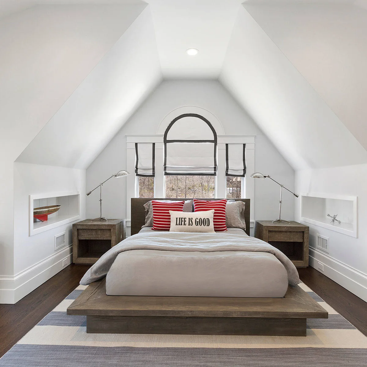 Attic bedroom with a low wood platform bed, red striped pillows and matching task lamps