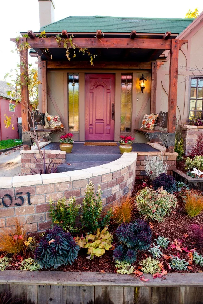 Red country door beneath timber pergola with glazed sidelights, side benches and curved brick garden wall