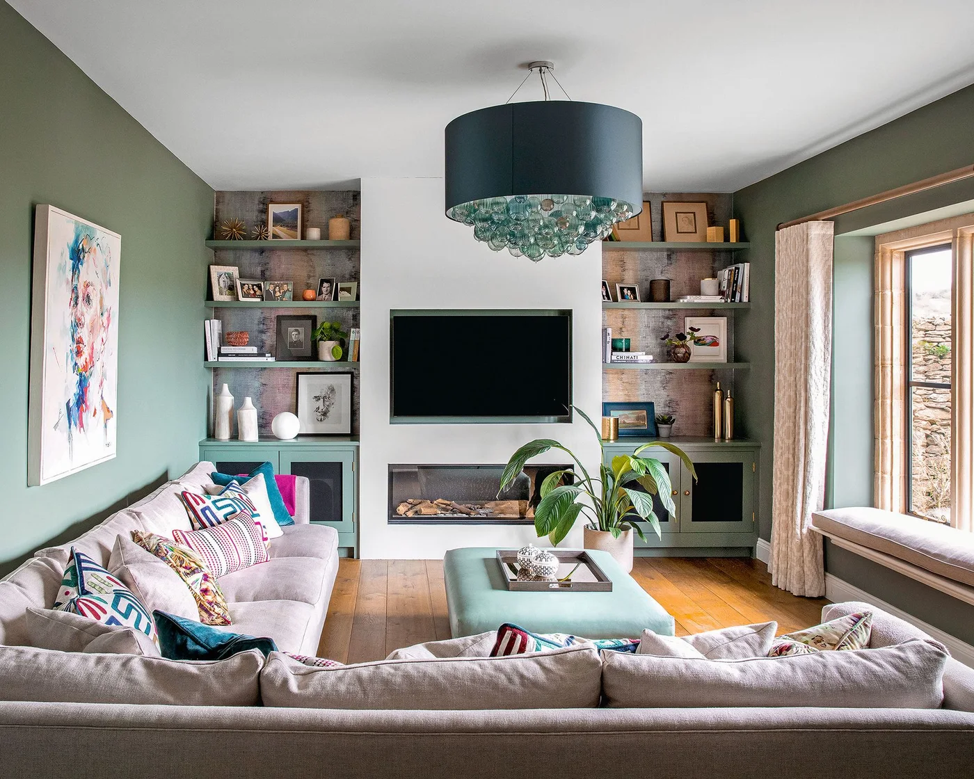 TV on a pale chimney breast between green alcove shelves in a green living room