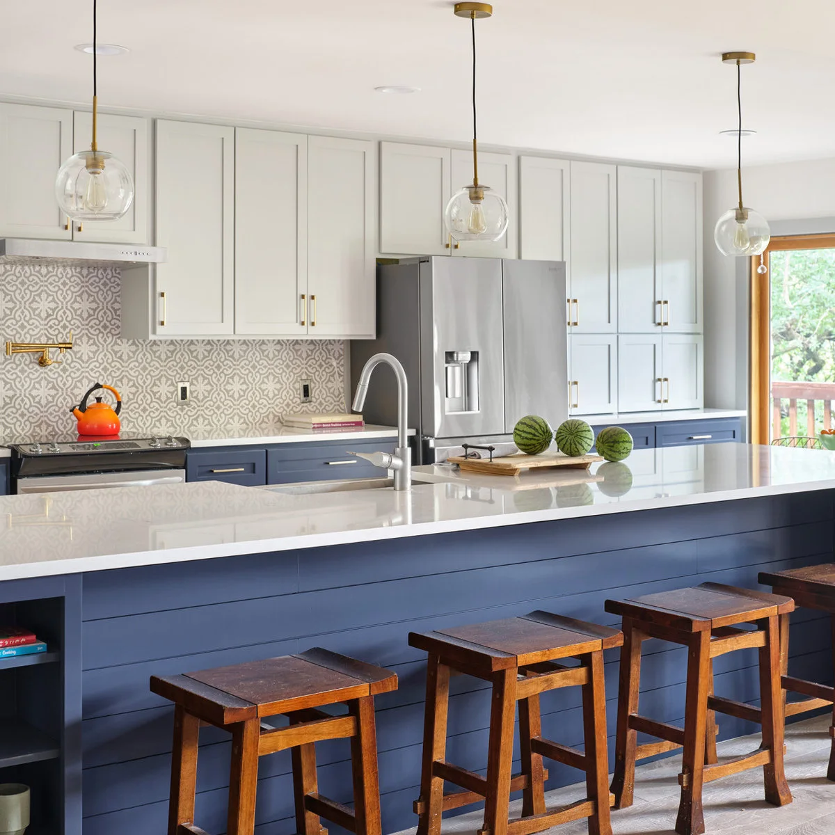 Navy lower cabinets and a peninsula sit beneath pale gray upper cabinets beside patterned tile, warm metal fittings and wood stools.