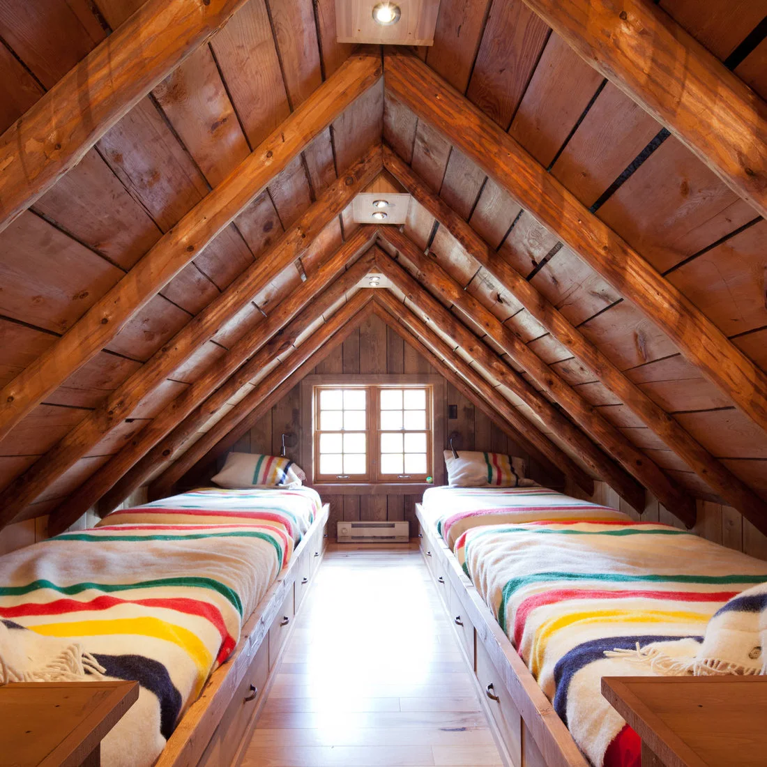 Two low timber beds with striped blankets beneath a sharply sloping timber roof