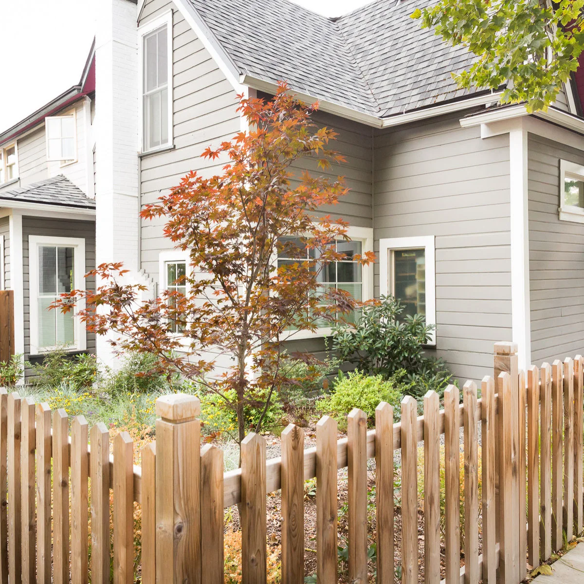 Natural wood pickets and capped posts beside a planted front garden and a pale-sided house.
