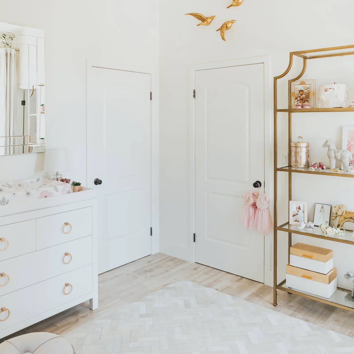 Nursery entrance with a white changing chest, closed doors and a gold-colored open display shelf