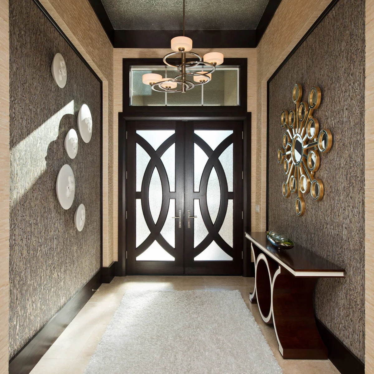 A dark curved-base console beneath a group of small round mirrors in a narrow patterned entrance.