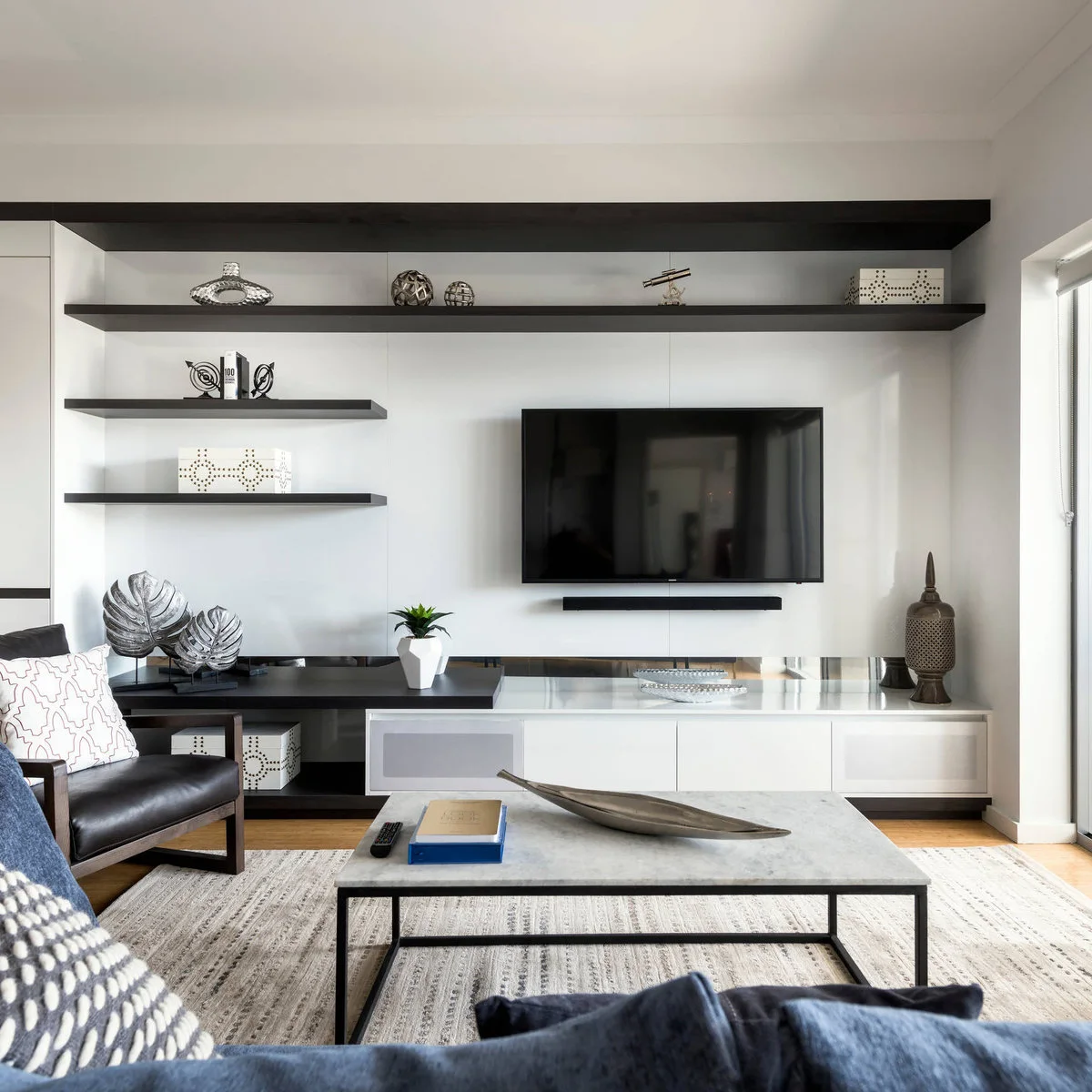 Long dark shelf carrying small sculptural objects above a television with shorter offset shelves to its left.