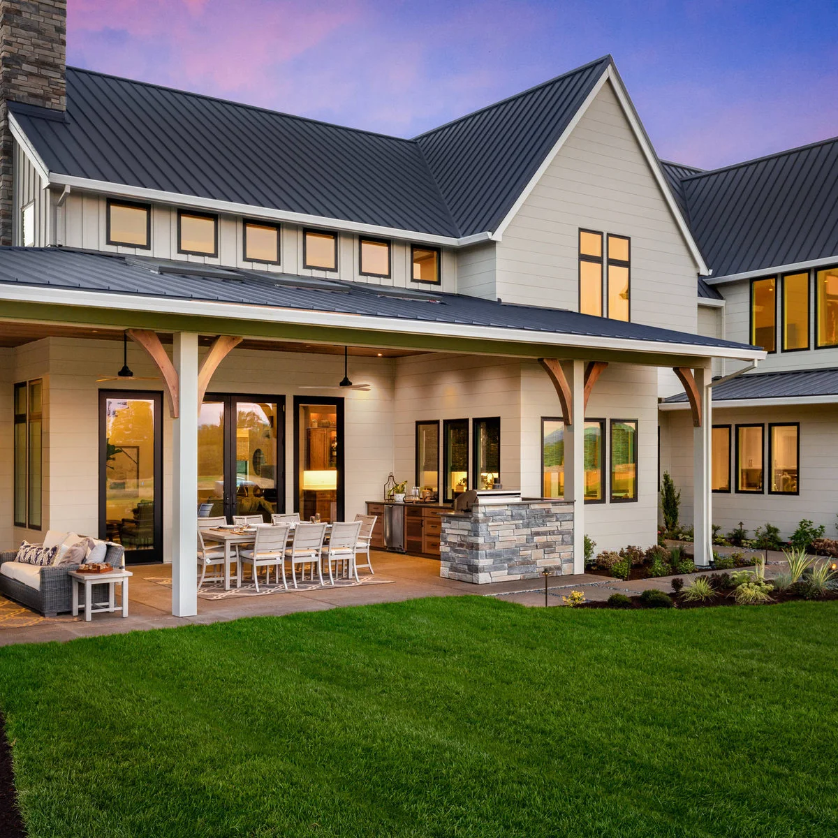 A shallow attached roof with white columns and curved wood brackets shelters a dining table beside glazed doors.