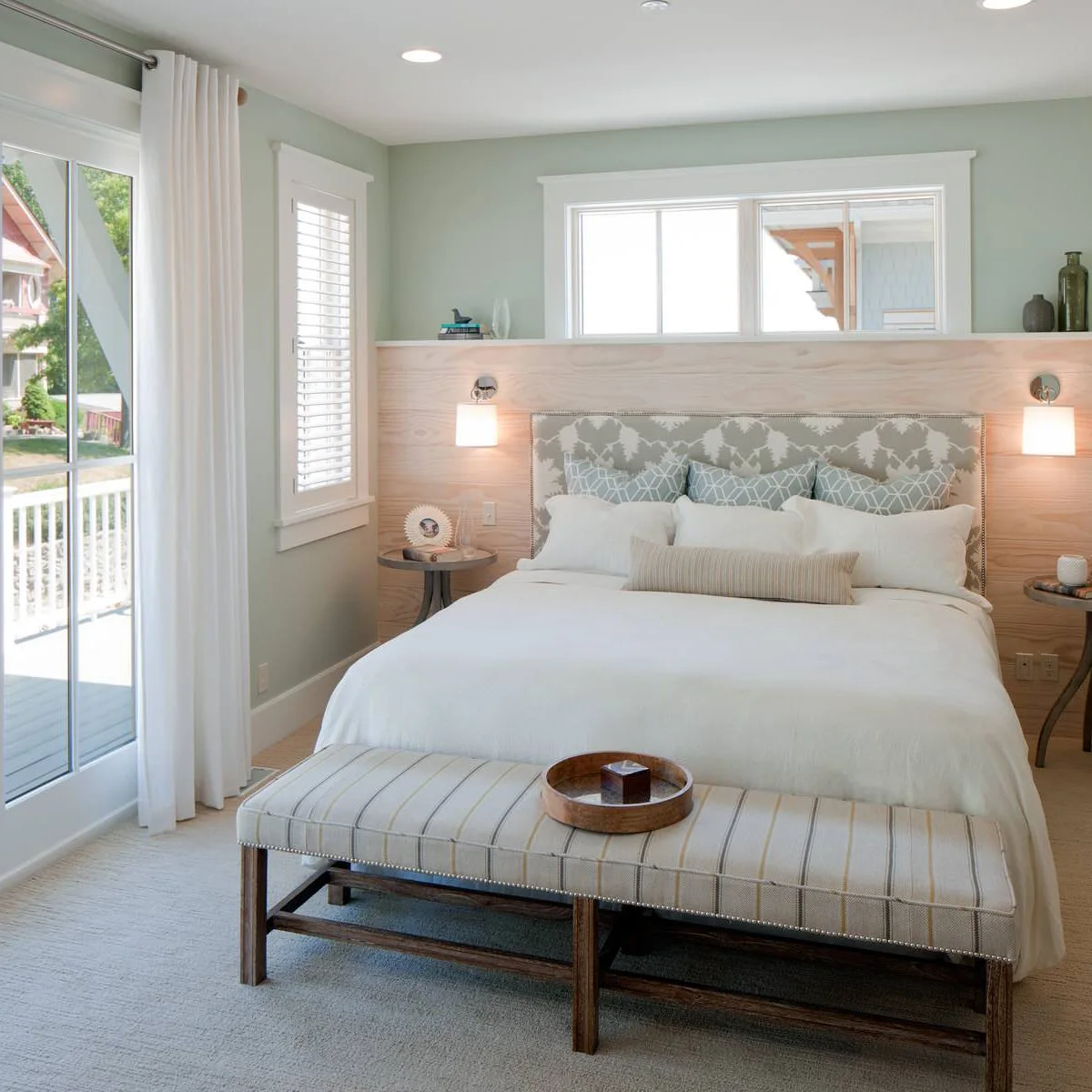 Two short metal wall lights with downward white shades sit beside a bed against pale green walls and light wood lower paneling.