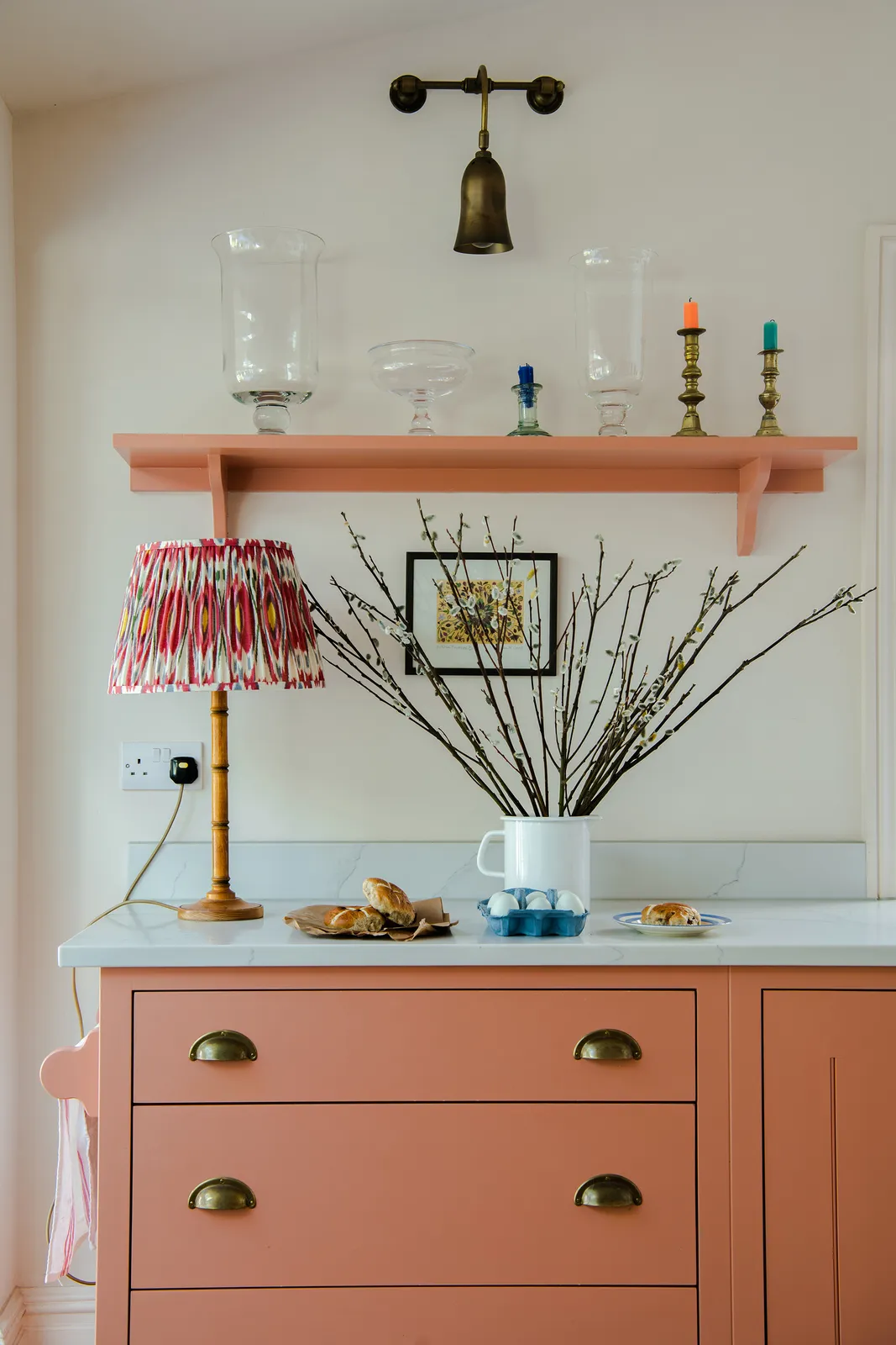 A coral cabinet with cup handles sits beneath a matching shelf and pale green wall
