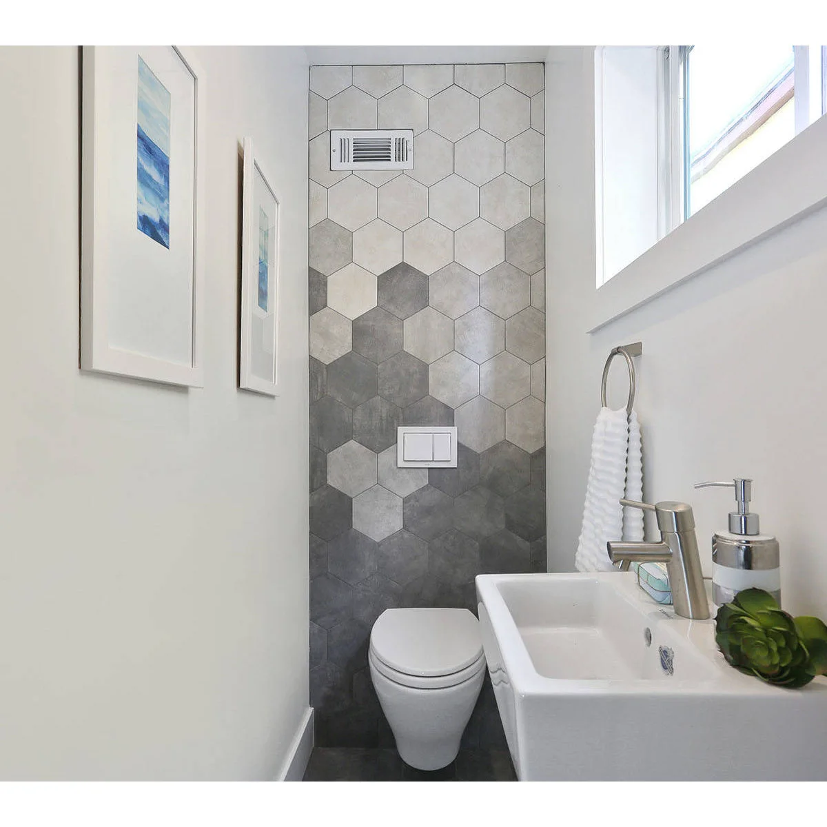 Gray hexagonal tiles behind a wall-hung toilet in a narrow white powder room with a compact basin.