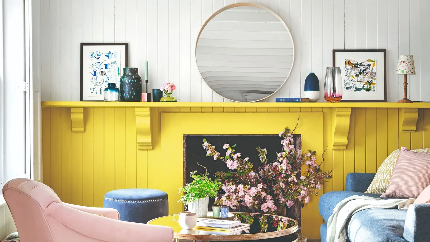 Yellow lower paneling and a long shelf sit below a white wall and round mirror between pink and blue seating