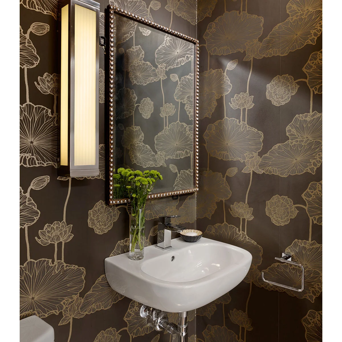 A compact white wall-mounted sink beneath a beaded mirror against brown walls with large floral outlines.
