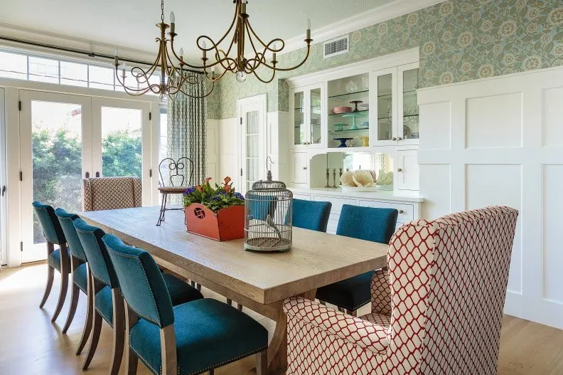Long wooden table with blue side chairs, patterned end chairs and white built-in dining storage.
