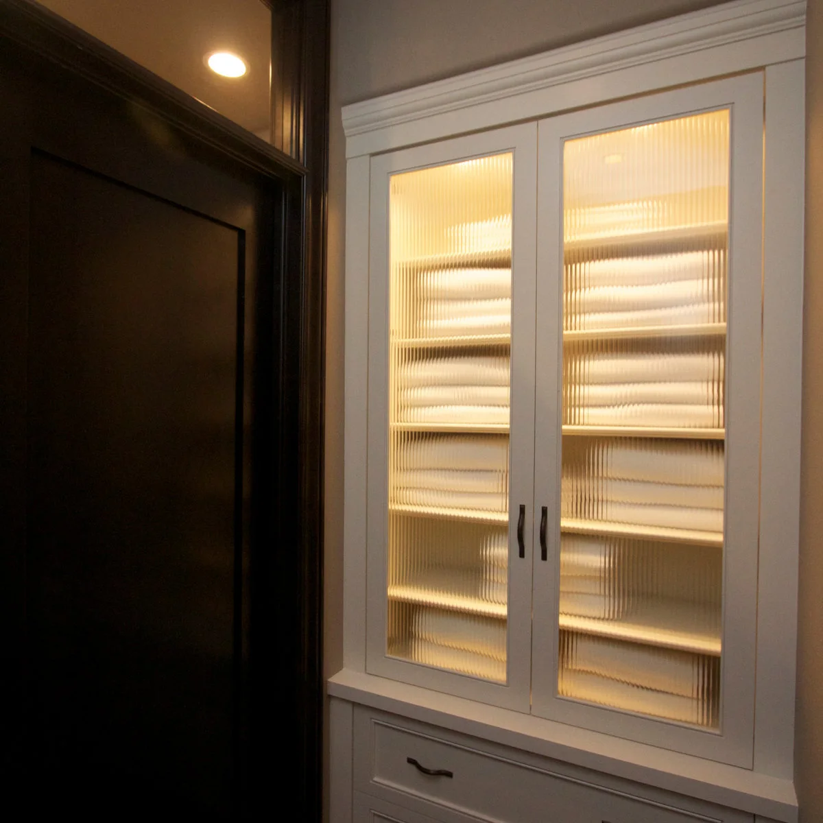 White linen cabinet with ribbed translucent glass doors, pale folded towels and lower drawers