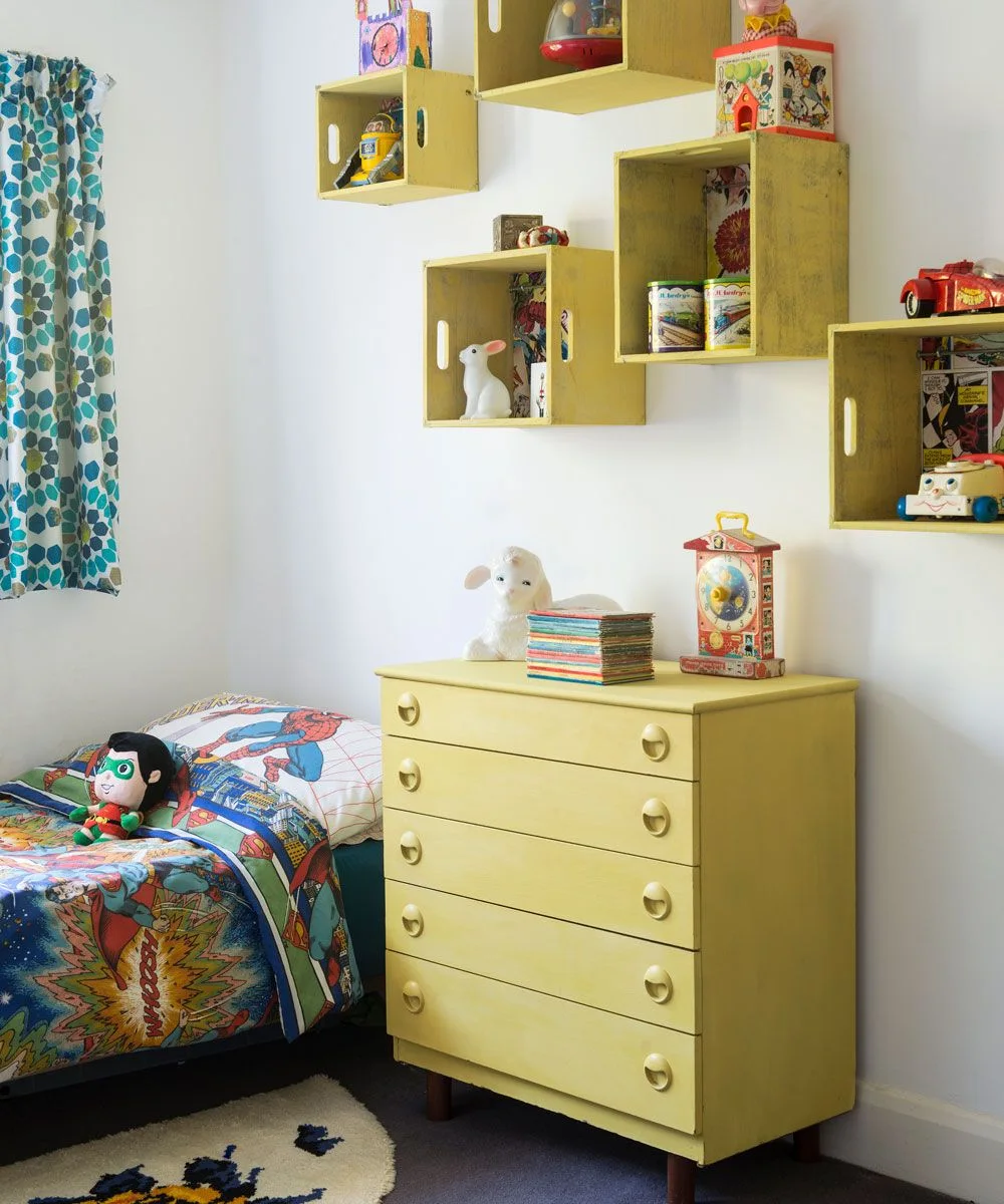 Yellow chest of drawers below yellow wall crates displaying a toy car, robot and decorative objects