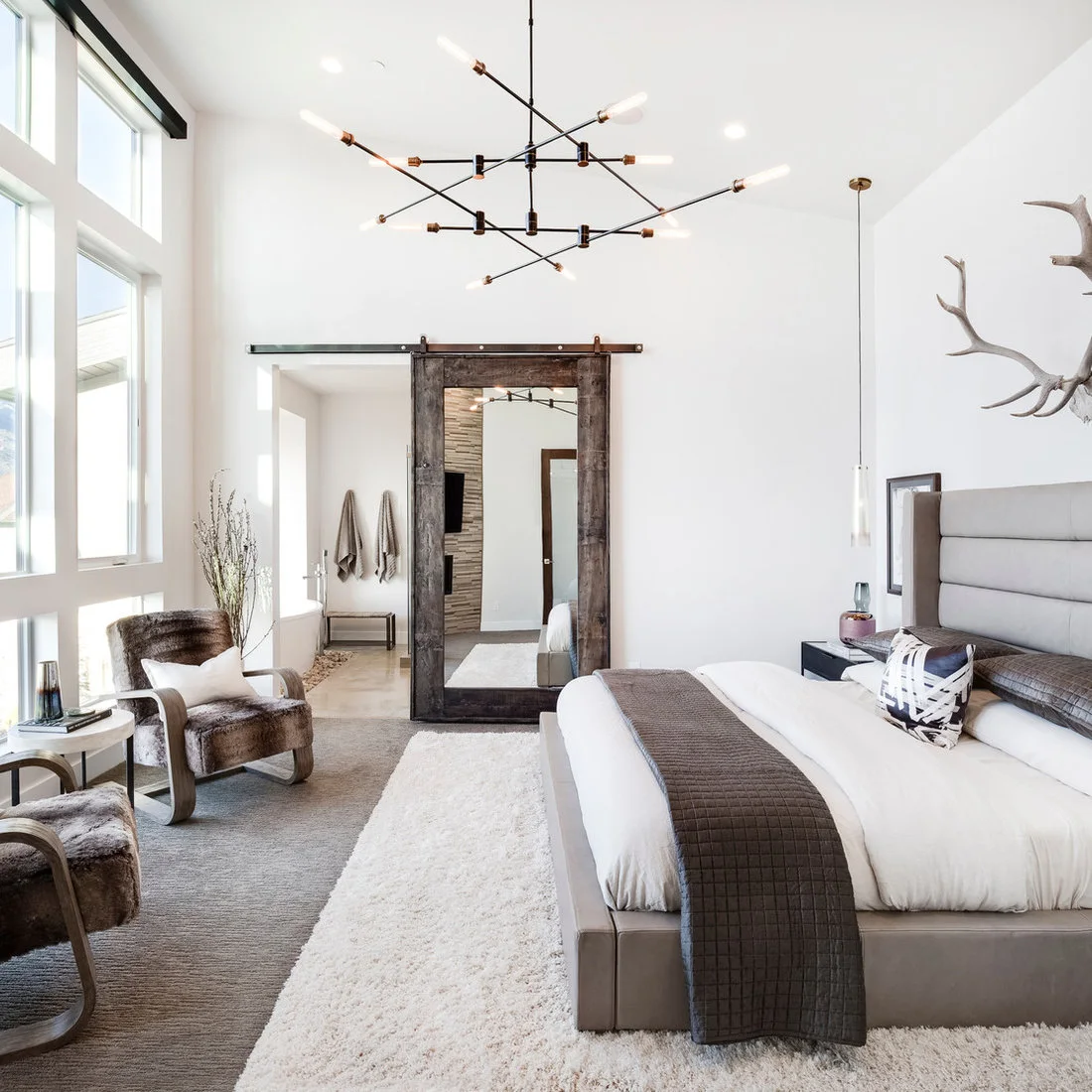A pale upholstered bed facing a rustic mirrored sliding door in a bright white bedroom