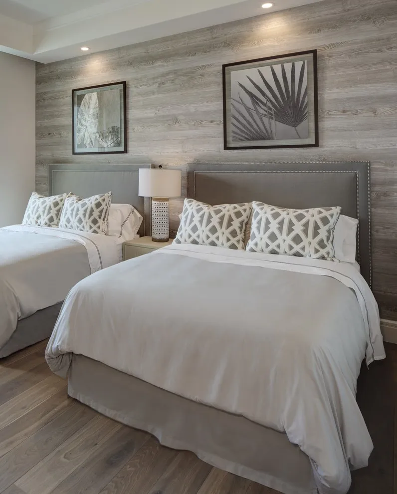 Gray horizontal timber grain forms a wall behind twin pale beds with patterned cushions