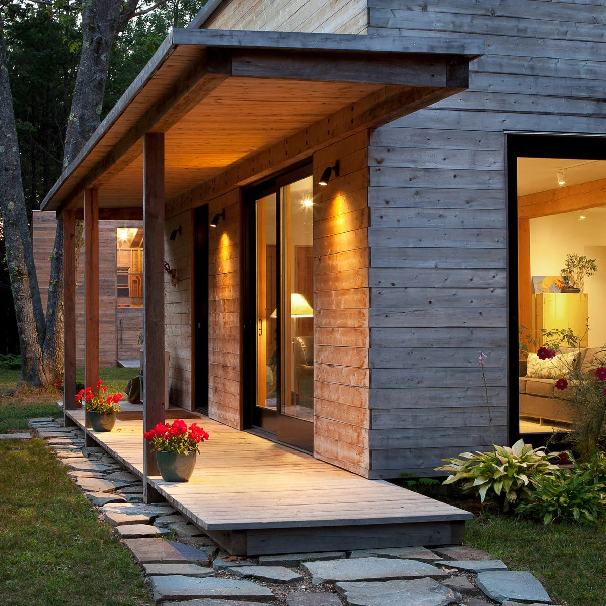 Small wood-sided home with a shallow covered front porch and two flower pots near its posts