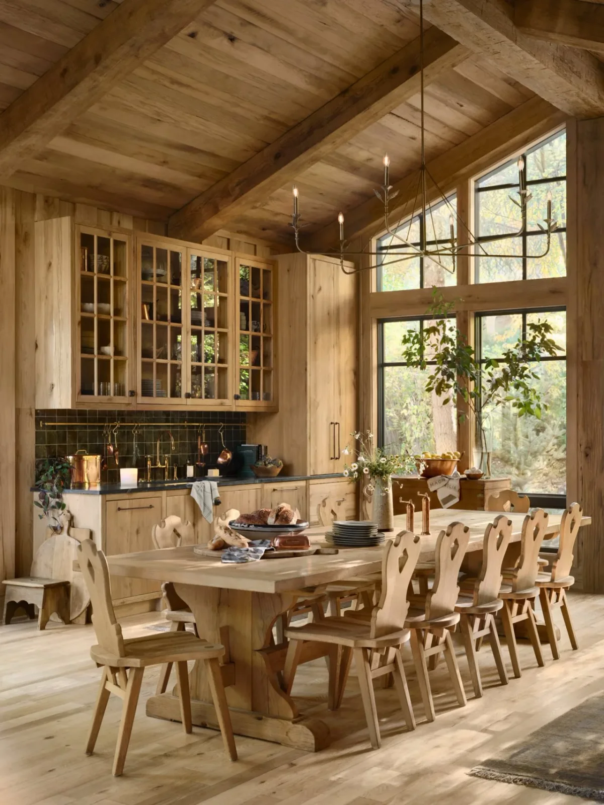 Glass-front wood cupboards stand against wood walls and a pitched wood ceiling, with a dark backsplash and a dining table nearby.