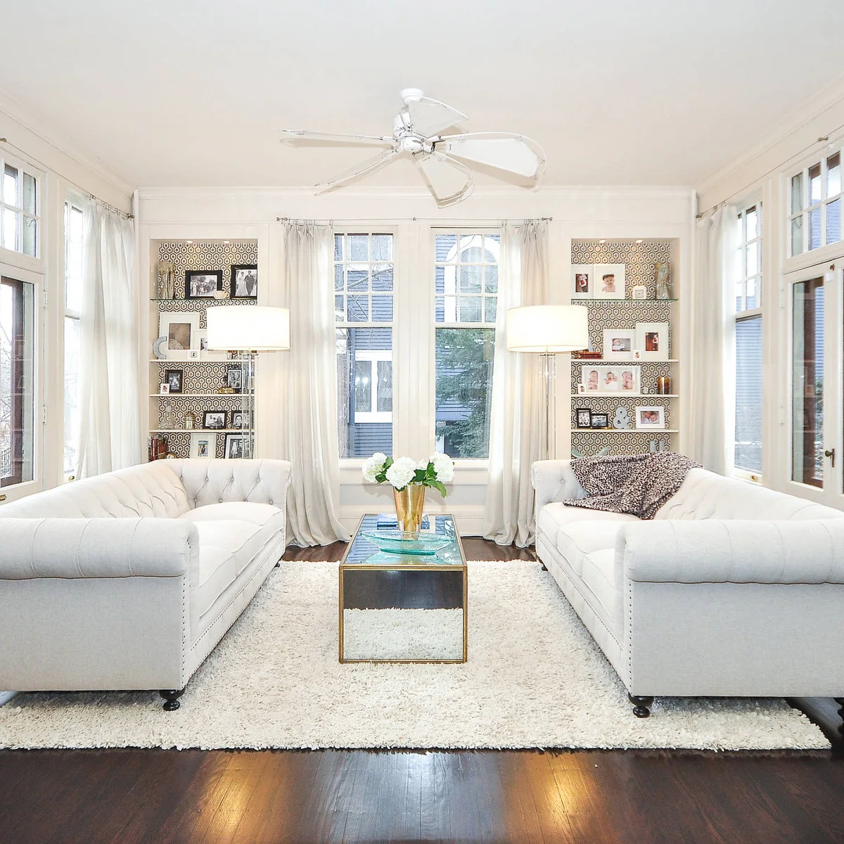 Two wallpaper-backed display recesses flank a window behind facing pale sofas.