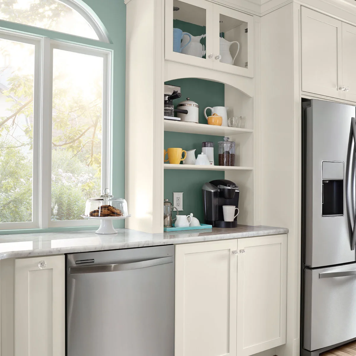 White kitchen coffee recess with open shelves, yellow mugs and a teal tray beside the refrigerator