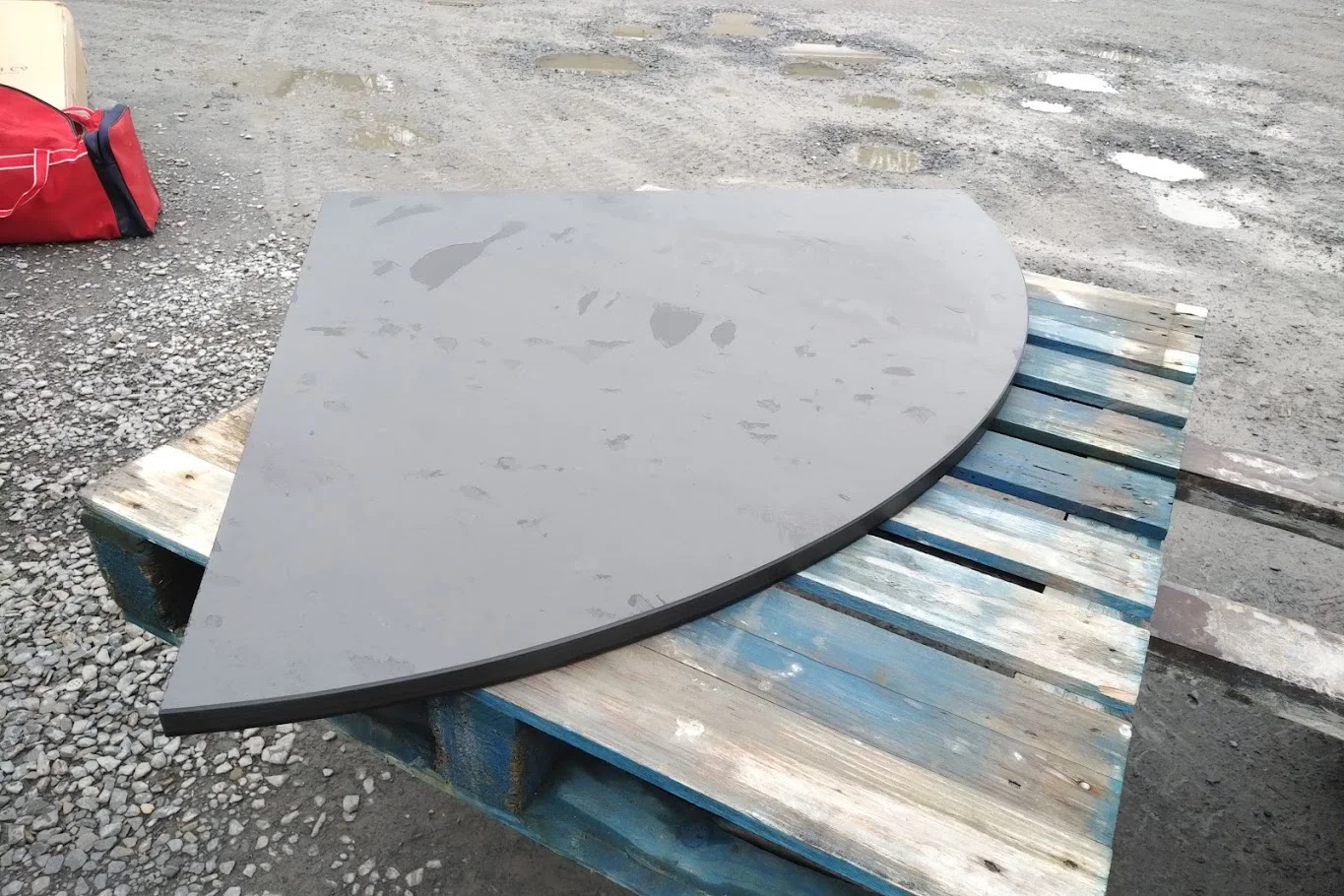 An uninstalled slate hearth with two straight back edges and a curved front rests on a pallet outdoors.