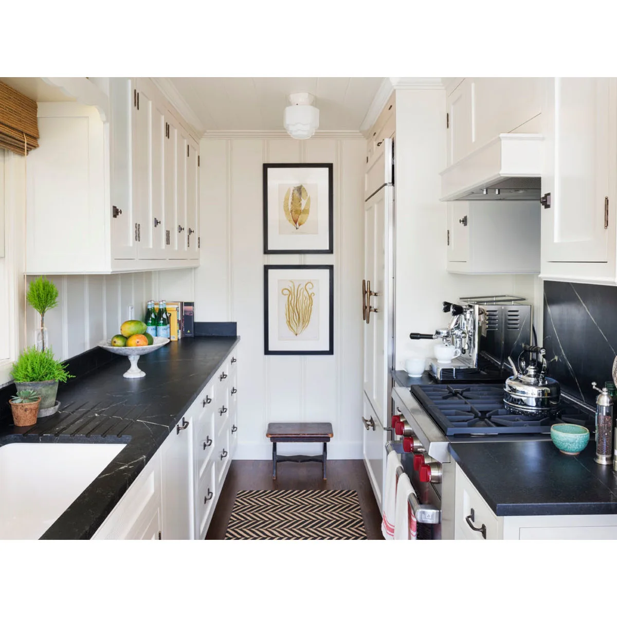 White galley kitchen with dark counters, base drawers and framed prints on the end wall