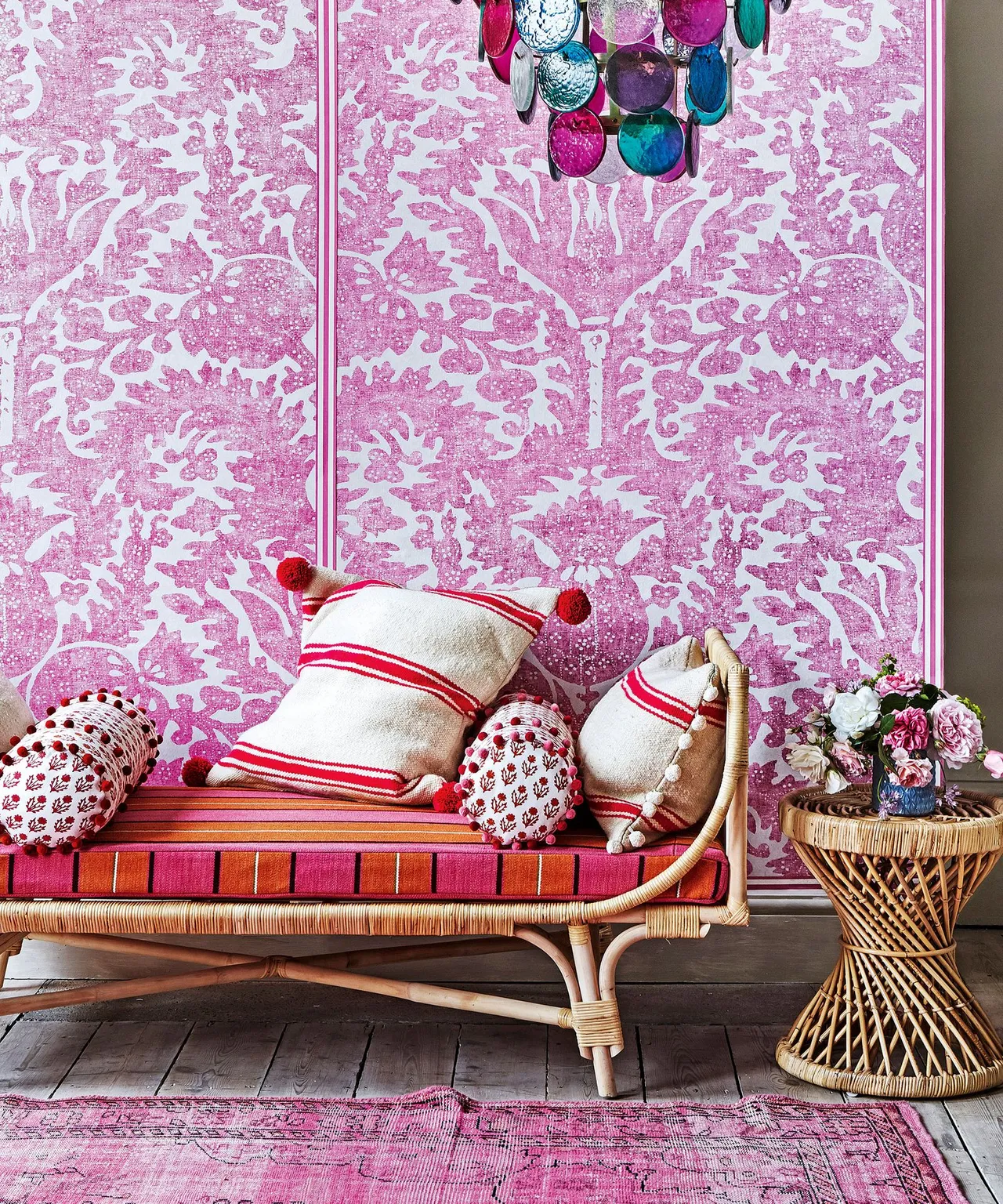 Sitting area with large pink wall pattern, woven sofa, striped cushion, red-and-white pillows, woven side table and pink rug.