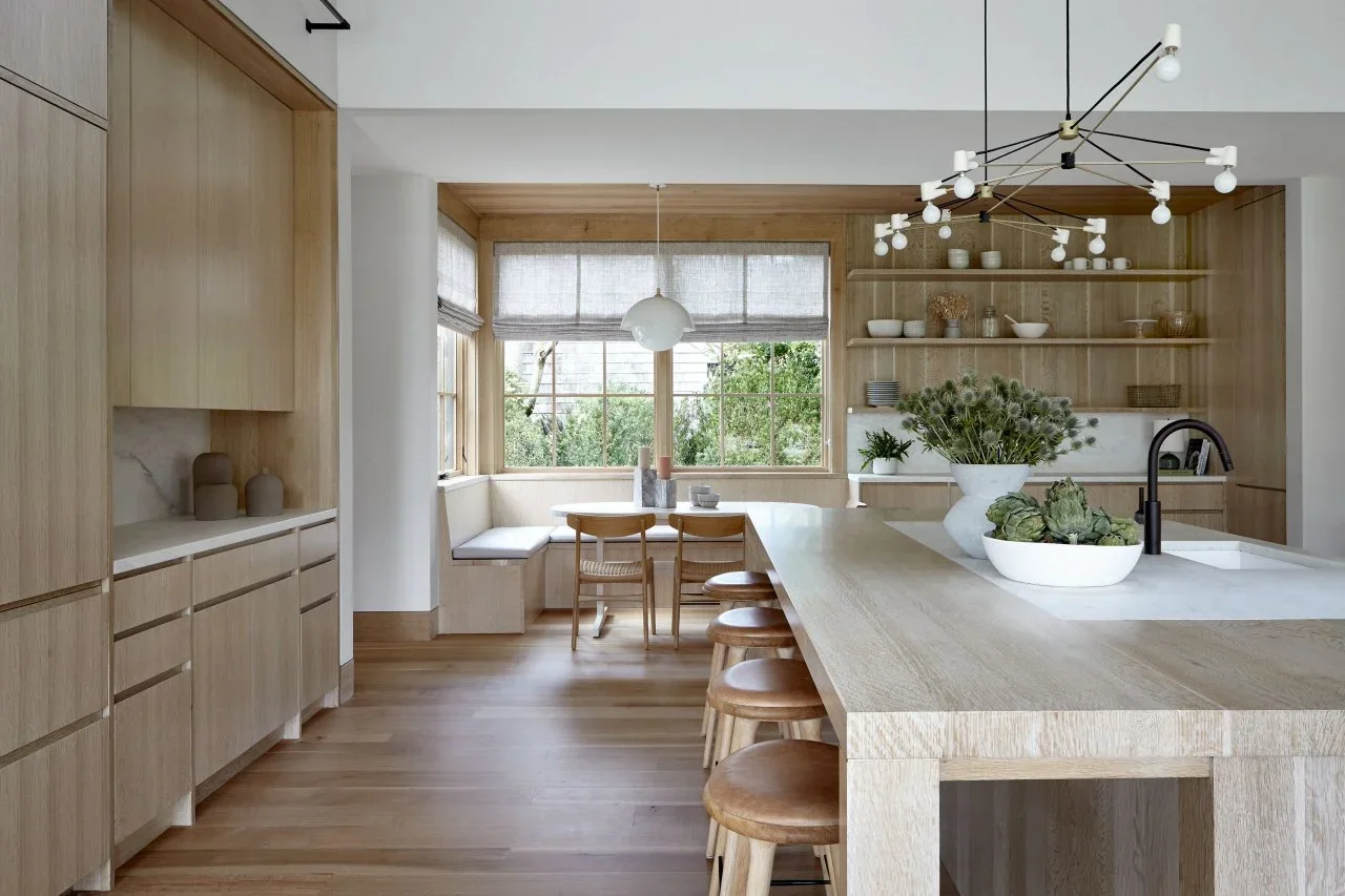 Pale flat wood cupboards, open shelves and a window banquette connect with a long pale island and wood stools.