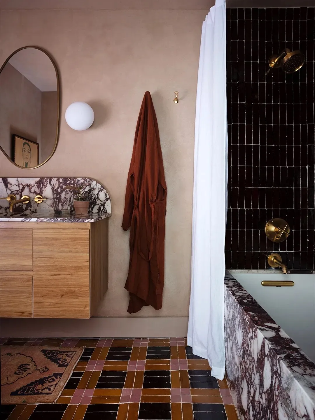 Brown, black and pink rectangular floor tiles sit beside a timber vanity and pink bathroom walls