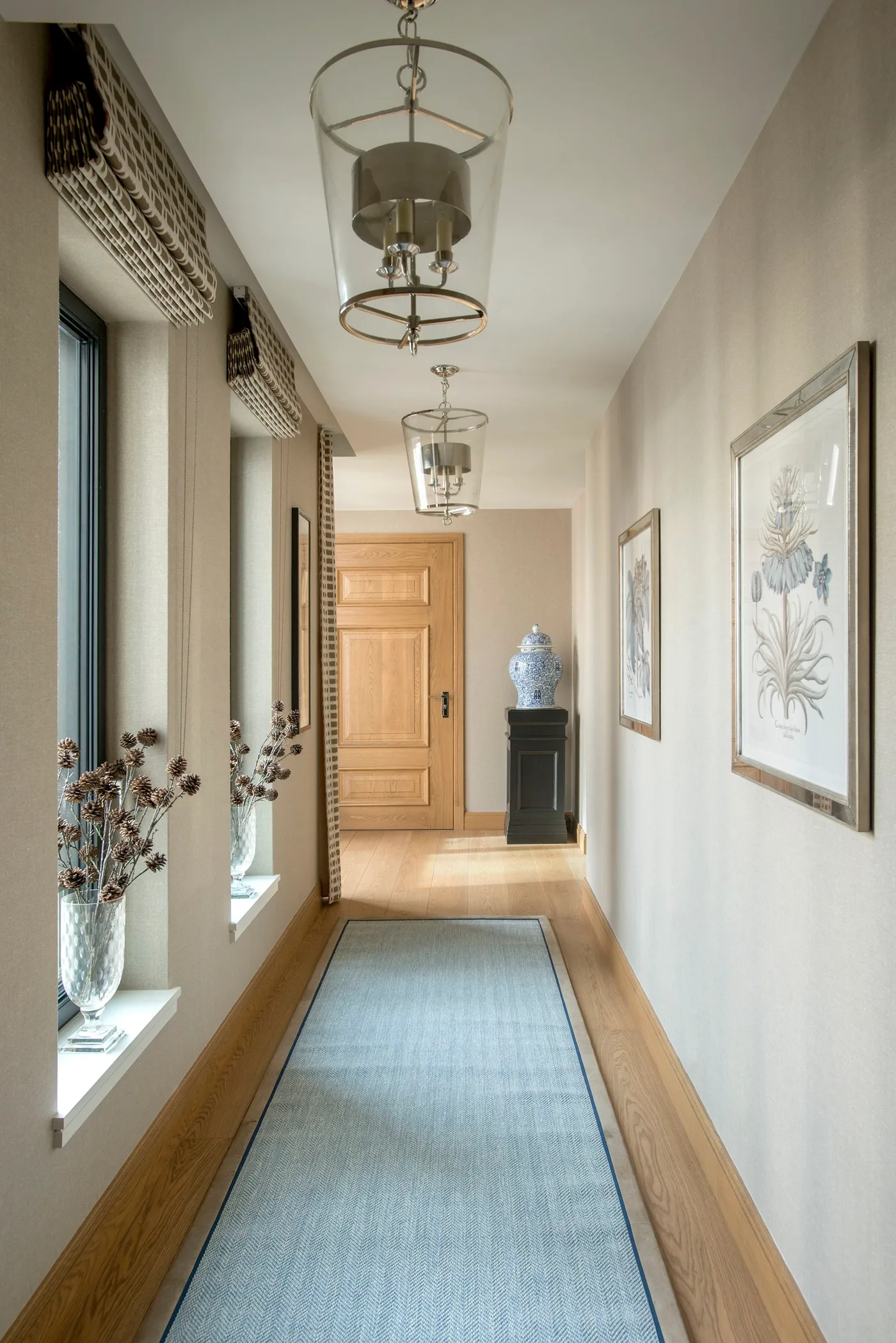Pale blue bordered runner in a light hallway with wood floor, window blinds, botanical pictures and repeated lanterns